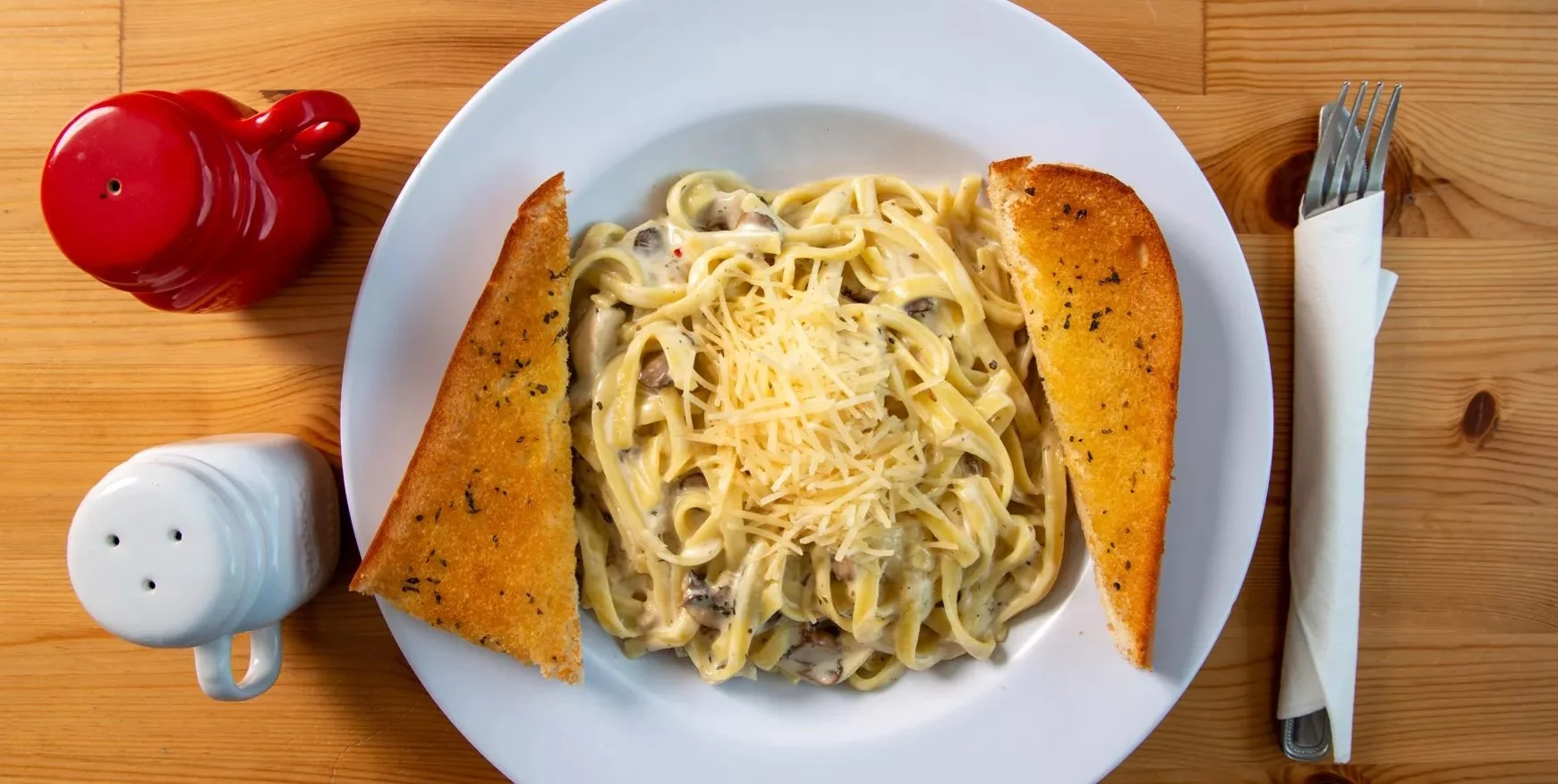 Plate of halal chicken fettuccine alfredo pasta topped with shredded parmesan and served with two slices of garlic bread at Castello Pizza & Pasta in Seattle.